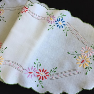 May include: White linen table runner with scalloped edges and embroidered flowers in shades of pink, yellow, red, and blue.