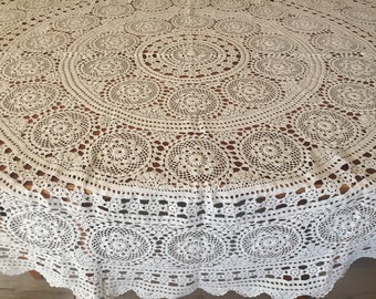 May include: A round, off-white, hand-crocheted tablecloth featuring an intricate, repeating circular floral pattern. The design includes a central medallion surrounded by concentric rings of lace motifs and a scalloped, decorative border.