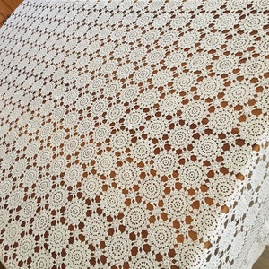 May include: A white crocheted tablecloth with a circular pattern. The tablecloth is laid out on a wooden table.