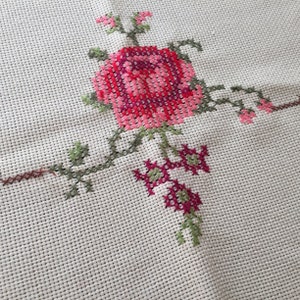 Puede incluir: Tela blanca con un dise&ntilde;o de punto de cruz de una rosa rosa y roja con hojas y tallos verdes.