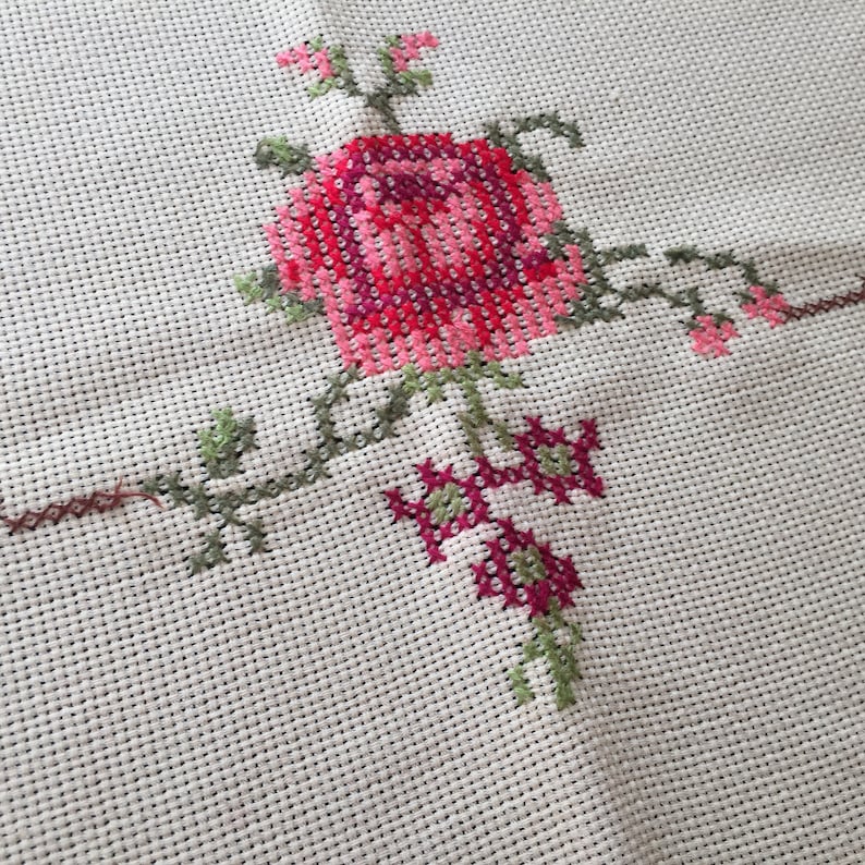 Puede incluir: Tela blanca con un dise&ntilde;o de punto de cruz de una rosa rosa y roja con hojas y tallos verdes.