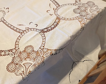 May include: White tablecloth with intricate embroidered lace detailing. The lace features a circular design with floral motifs.