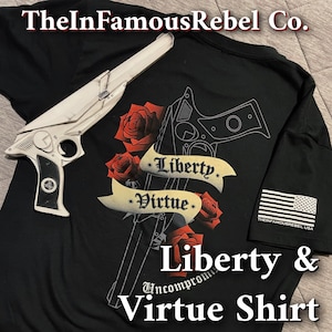 May include: Black t-shirt with a white gun graphic, roses, and the words "Liberty" and "Virtue." A white prop gun is placed on the shirt. The shirt also features the text "Liberty & Virtue Shirt" and an American flag.