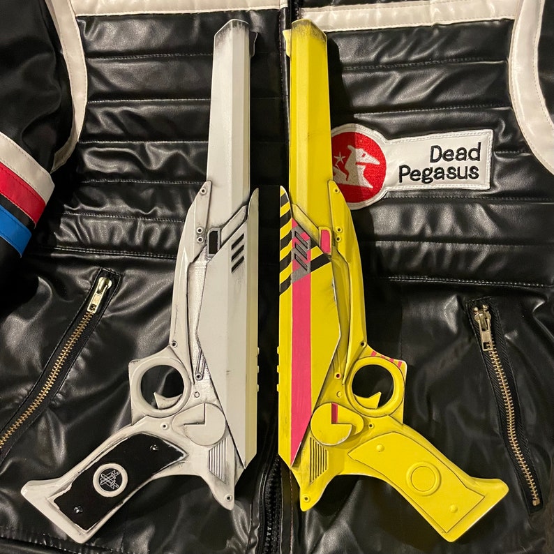 Two 3D printed ray gun props one painted like Party Poisons weapon from Danger Days music videos, one in white with black grips. Both laid side by side on top of a Party Poison cosplay jacket. Perfect for MCR fans, collectors & cosplay enthusiasts