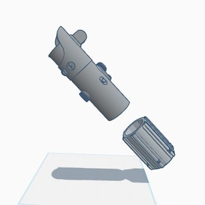 May include: A grey lightsaber hilt, with a cylindrical design and detailed accents, is shown disassembled. The hilt is composed of two parts, with the top section featuring a curved guard and several buttons.
