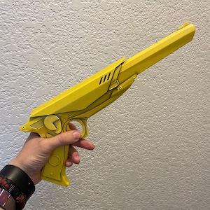 May include: A yellow, futuristic-style pistol with a long barrel and intricate detailing. The gun features a trigger, grip, and a circular design element. The overall design is angular and stylized, with a matte finish.