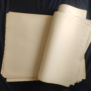 May include: A stack of blank, off-white paper sheets, folded in half and lying on a dark blue surface.