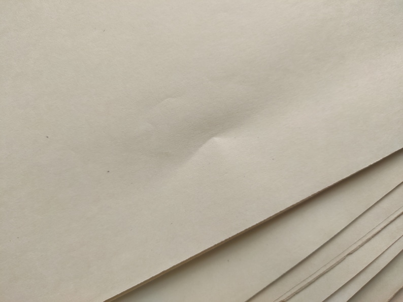 May include: A stack of off-white paper sheets. The top sheet has a slight crease in the center.