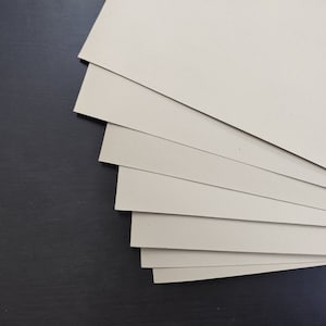 May include: A stack of beige cardstock paper sheets, arranged in a fan shape, against a black background.