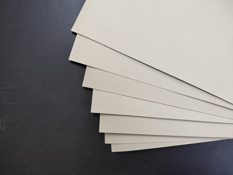 May include: A stack of beige cardstock paper sheets, arranged in a fan shape, against a black background.