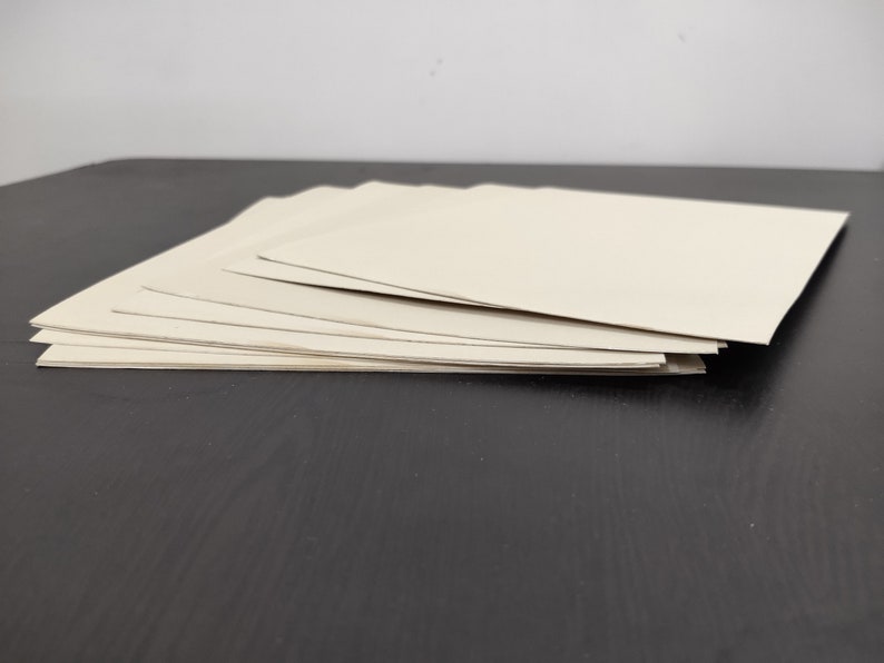 May include: A stack of eight off-white cardstock sheets on a black surface.