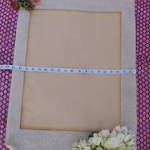 Op de afbeelding: Een beige stoffen frame met een bruine papieren insert. Het frame is versierd met roze en witte bloemen. Bovenaan de afbeelding is een meetlint zichtbaar.