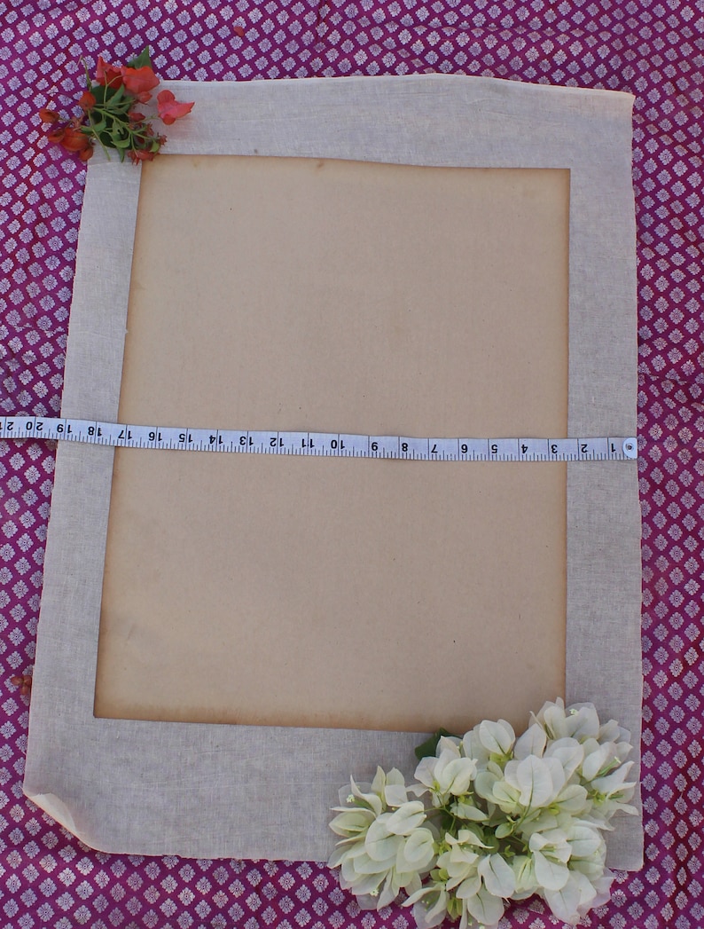 Op de afbeelding: Een beige stoffen frame met een bruine papieren insert. Het frame is versierd met roze en witte bloemen. Bovenaan de afbeelding is een meetlint zichtbaar.