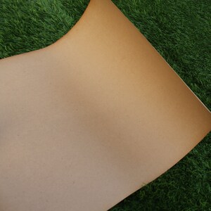 Op de afbeelding: Een vel bruin kraftpapier met een licht getextureerd oppervlak. Het papier ligt op een bed van groen kunstgras.