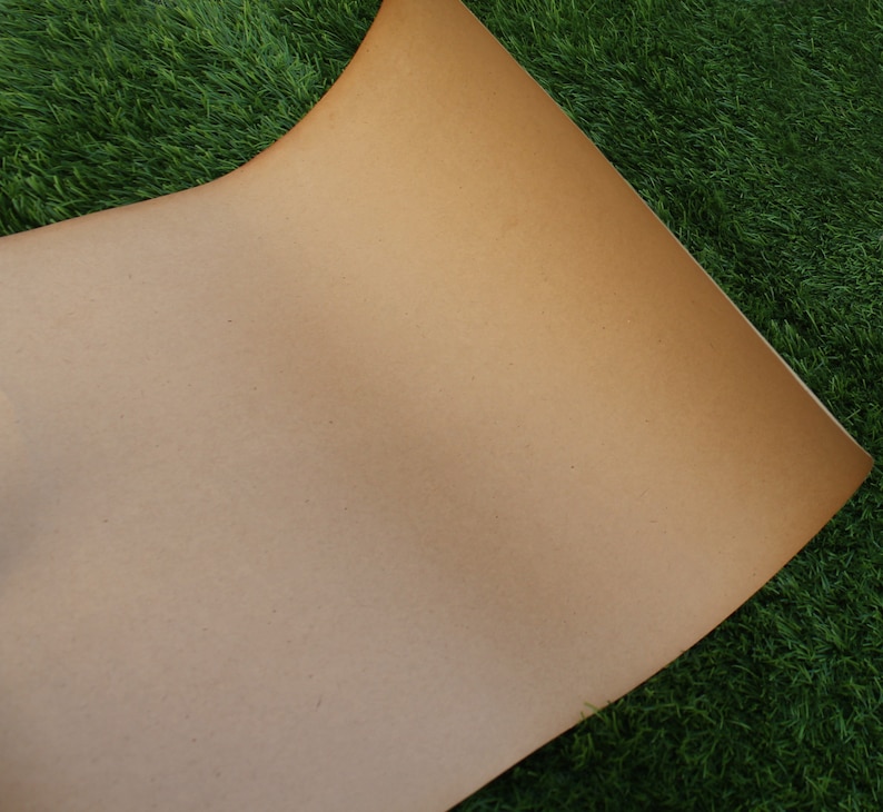 Op de afbeelding: Een vel bruin kraftpapier met een licht getextureerd oppervlak. Het papier ligt op een bed van groen kunstgras.