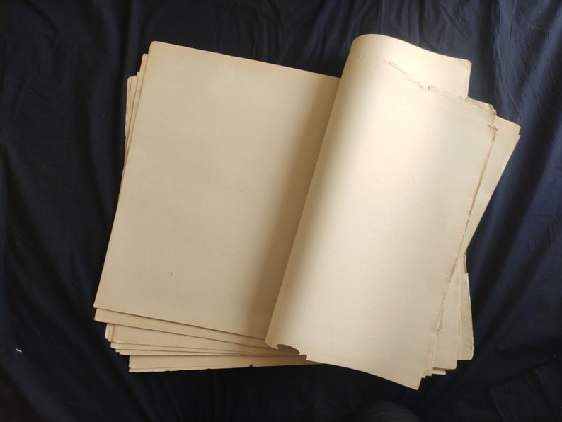 May include: A stack of blank, off-white paper sheets, folded in half and lying on a dark blue surface.