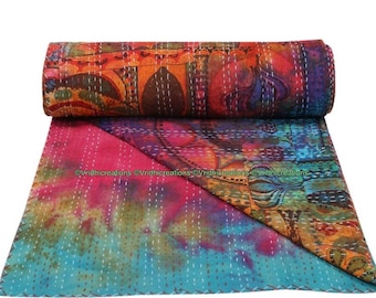 Puede incluir: Una colcha rectangular con una sección enrollada y otra desplegada. La parte superior muestra un patrón multicolor vibrante en tonos naranja, rojo y azul. La parte inferior presenta un efecto tie-dye en rosa y turquesa con costuras blancas.