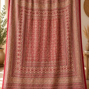Puede incluir: Un tapiz rectangular de tela con una base de color rojo intenso y patrones geom&eacute;tricos y florales repetitivos en tonos crema y marr&oacute;n apagado. La tela presenta un dise&ntilde;o de bordes superpuestos con l&iacute;neas de costura verticales visibles.