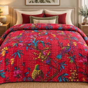 May include: A vibrant red quilted bedspread featuring a detailed botanical print with colorful birds, green foliage, and yellow flowers. The fabric displays a visible white running stitch pattern throughout, creating a textured, layered appearance.