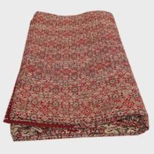Puede incluir: Un textil plegado que presenta un patr&oacute;n denso y repetitivo de formas geom&eacute;tricas y florales en tonos rojo oscuro, crema y marr&oacute;n oscuro. La tela muestra motivos sim&eacute;tricos intrincados en toda su superficie, con un borde dobladillado visible.