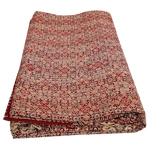 Peut inclure: Un tissu en coton rouge et crème avec un motif répétitif de petits cercles et d'étoiles. Le tissu est plié en deux et les bords sont visibles.