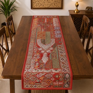 May include: A rectangular table runner featuring a vibrant red base with an intricate patchwork design. The fabric displays a variety of colorful, detailed patterns, including floral motifs, geometric shapes, and ornate embroidery with metallic accents.