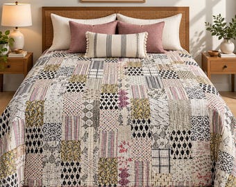 May include: A patchwork quilt featuring a variety of rectangular fabric blocks with diverse patterns in shades of black, white, yellow, and pink. The quilt is layered with two large cream pillows, two dusty rose pillows, and a central lumbar pillow.