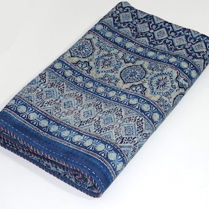 May include: A blue and white kantha quilt with a geometric pattern. The quilt is folded in half and has a red stitching detail around the edges.
