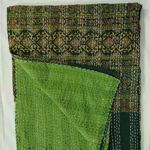 Op de afbeelding: Een groene kantha-deken met een patroon. De deken is dubbelgevouwen en heeft witte stiksels.