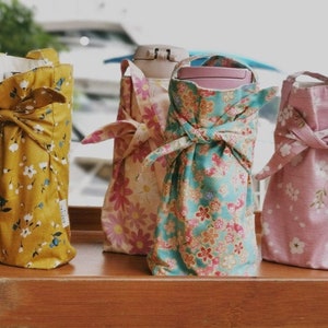 Puede incluir: Cuatro porta botellas de agua cubiertos de tela con patrones florales. Los porta botellas son de color amarillo, rosa, azul y rosa con patrones florales blancos.