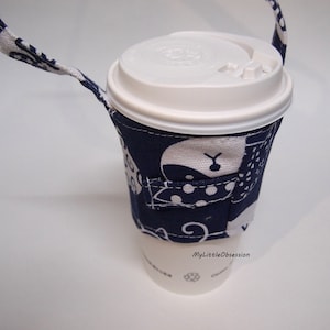 Puede incluir: Una taza de café desechable blanca con tapa blanca, dentro de una funda de tela azul marino. La funda tiene un estampado de oso blanco y una correa. El texto "MyLittleObsession" es visible en la taza.
