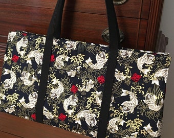 May include: A rectangular fabric tote bag featuring a black background with a repeating pattern of white koi fish, gold swirling water motifs, yellow maple leaves, and small red square accents. The bag has two long black woven shoulder straps.
