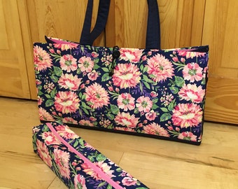 May include: A rectangular tote bag and a matching long, narrow zippered case, both featuring a dark blue fabric with a vibrant pink and white floral pattern. The tote has two dark blue shoulder straps and a central toggle closure mechanism.