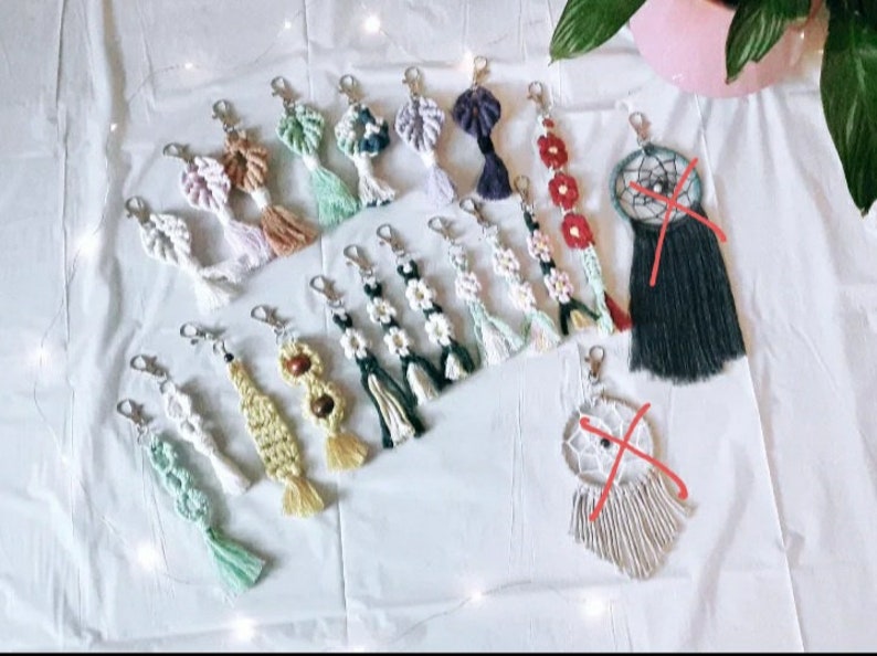 May include: A collection of colorful macrame keychains with various designs, including flowers, dreamcatchers, and geometric patterns. The keychains are made with natural fibers and have tassels.