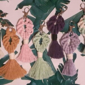 May include: Seven colorful macrame keychains with tassels. The keychains are made with different colored yarn and feature a variety of patterns.