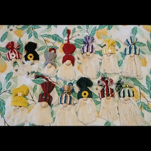 May include: A collection of 12 handmade gnome ornaments with various colored hats and white beards. The gnomes are made with yarn and have a wooden bead for the head. The hats are decorated with stars, flowers, and other embellishments.