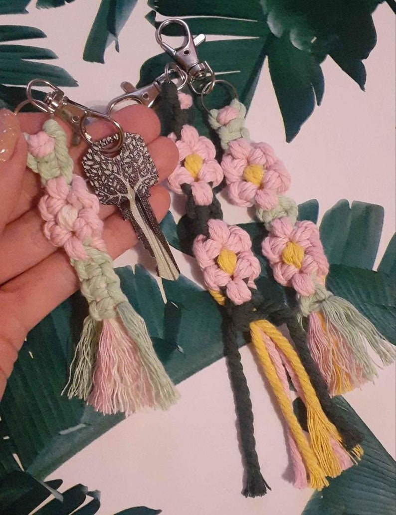 May include: Three handmade macrame keychains with pink, green, and yellow tassels. Each keychain features a flower design with pink and yellow accents.
