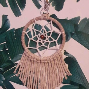 May include: A beige dreamcatcher keychain with a white web and a brown bead in the center. The keychain has a silver clip.