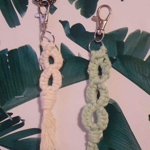 May include: Two handmade macrame keychains with tassels. One keychain is cream colored and the other is light green.