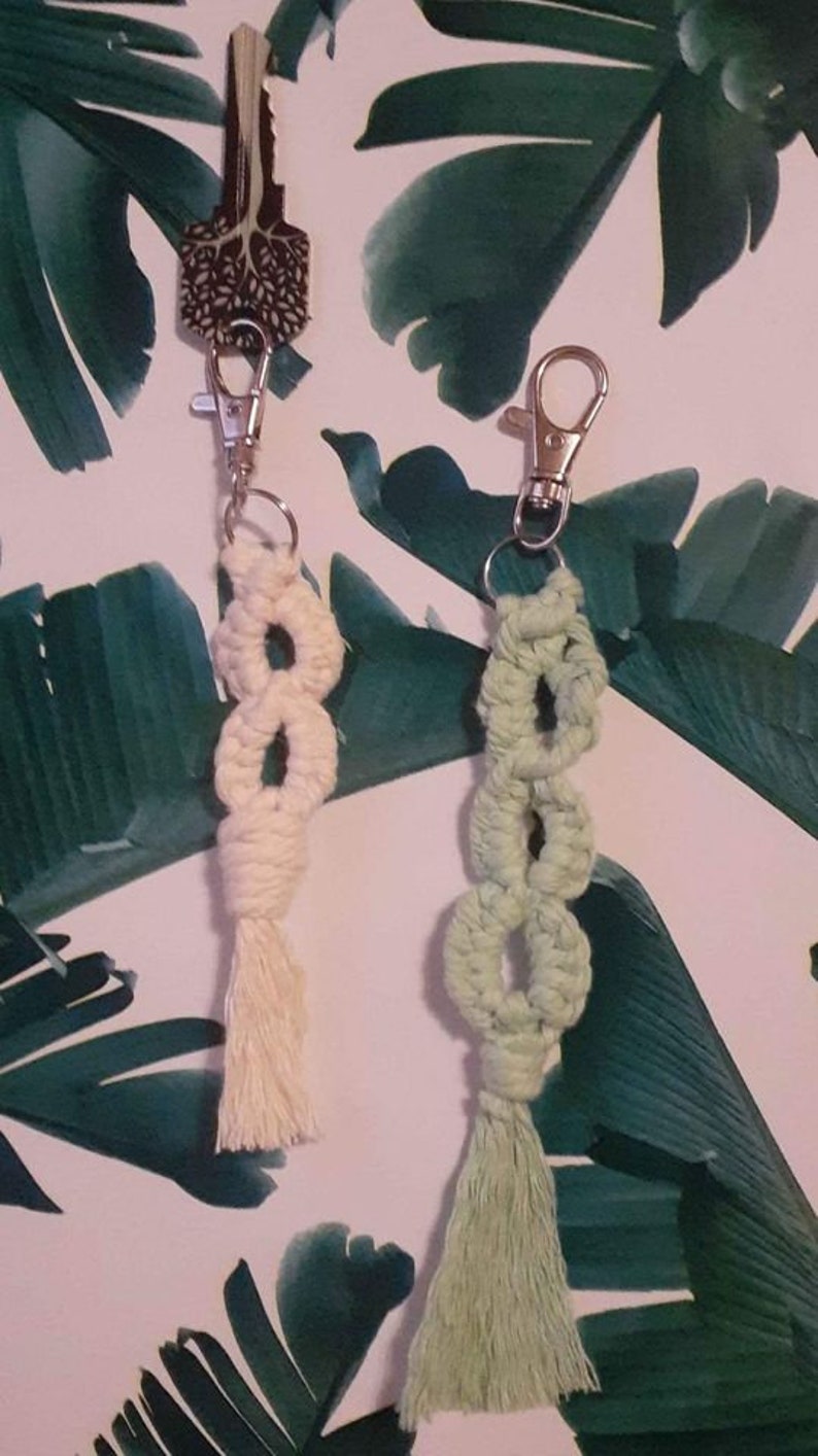 May include: Two handmade macrame keychains with tassels. One keychain is cream colored and the other is light green.