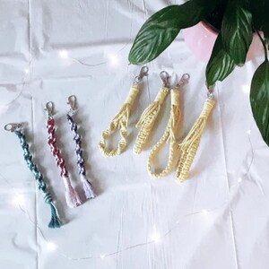 May include: A collection of six colorful handmade keychains. The keychains are made of braided yarn and have tassels. The keychains are in various colors, including blue, green, red, and yellow.