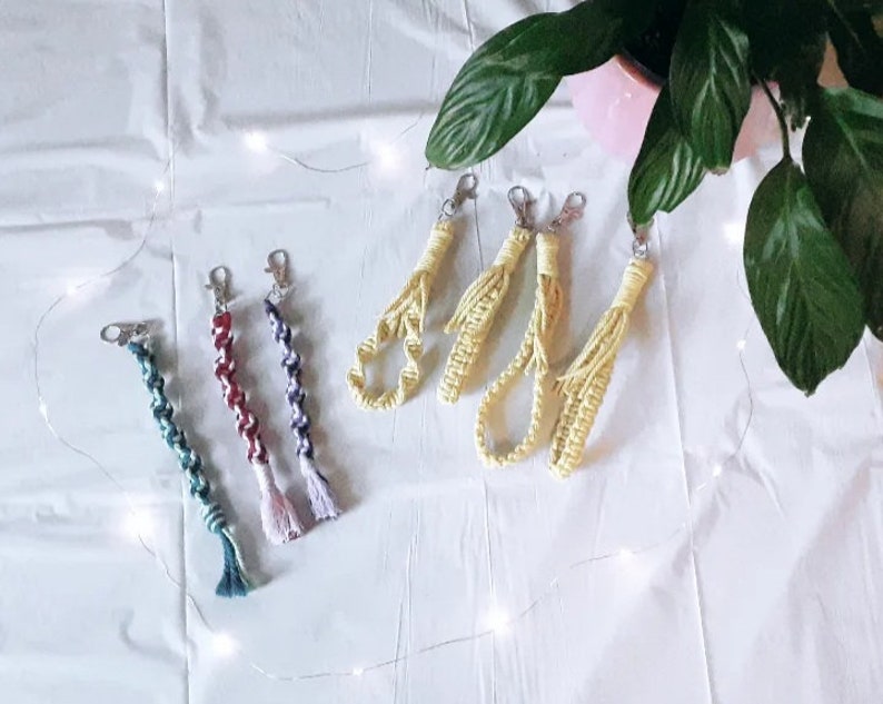 May include: A collection of six colorful handmade keychains. The keychains are made of braided yarn and have tassels. The keychains are in various colors, including blue, green, red, and yellow.