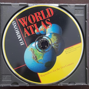 May include: A CD-ROM for a World Atlas by Hammond, in a clear plastic case. The disc features a black background with the words "WORLD ATLAS" in red and images of globes. The text "Mapmakers for the 21st Century" is also visible.