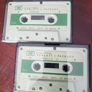 May include: A white ceramic mug with a black handle and the text "But First, Coffee" in a bold, black font. The mug is set against a blurred background, suggesting a cozy setting.