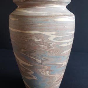May include: A tall, ceramic vase with a marbled design. The vase features a mix of colors, including light blue, brown, and cream, creating a swirling pattern. The vase has a wide base that tapers upwards, with a slightly flared rim. The overall height is approximately 10 inches.