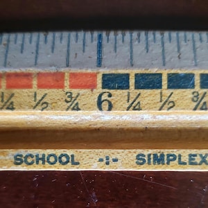 May include: A close-up of a wooden ruler with black and orange markings. The ruler is labeled "SCHOOL -- SIMPLEX" and shows measurements from 1/2 inch to 7 1/2 inches.