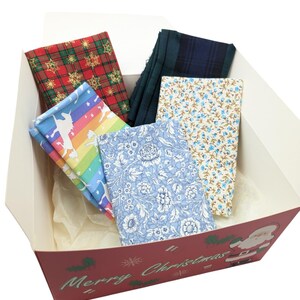 May include: A red and white Christmas gift box with a Santa Claus design. The box is filled with colorful fabric squares, including a rainbow unicorn print, a blue floral print, a blue and white plaid print, and a red and gold snowflake print.