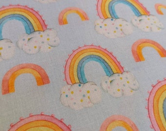 Peut inclure: Un tissu bleu clair avec un motif répété d'arcs-en-ciel colorés avec des nuages blancs et des pois roses.