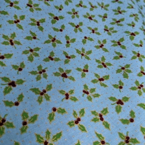 May include: A blue fabric with a repeating pattern of green holly leaves and red berries. The background is a light blue with a subtle gold glitter pattern.