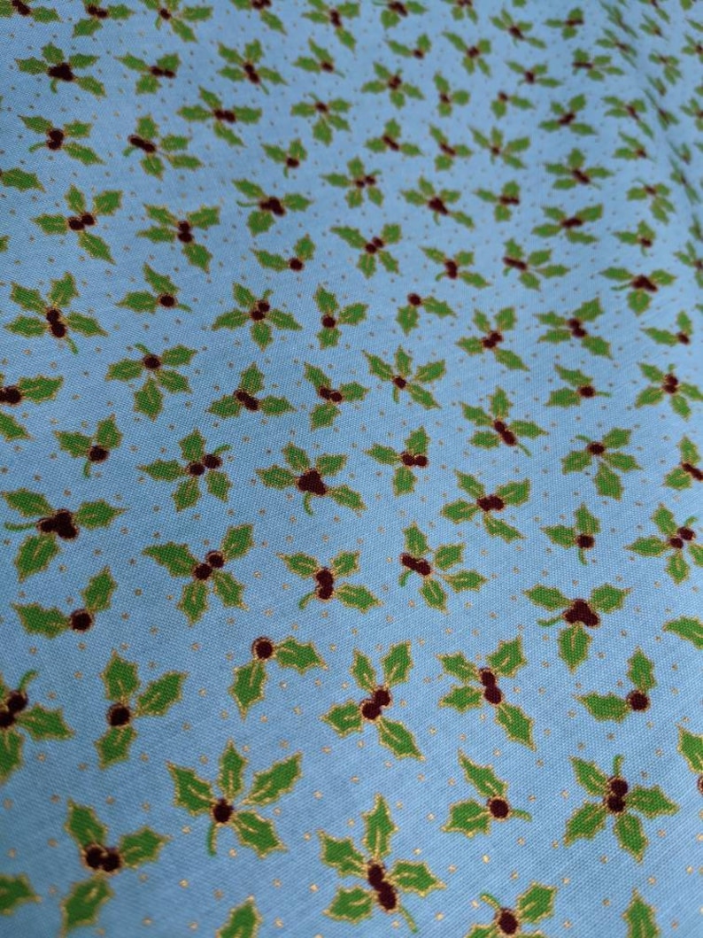 May include: A blue fabric with a repeating pattern of green holly leaves and red berries. The background is a light blue with a subtle gold glitter pattern.